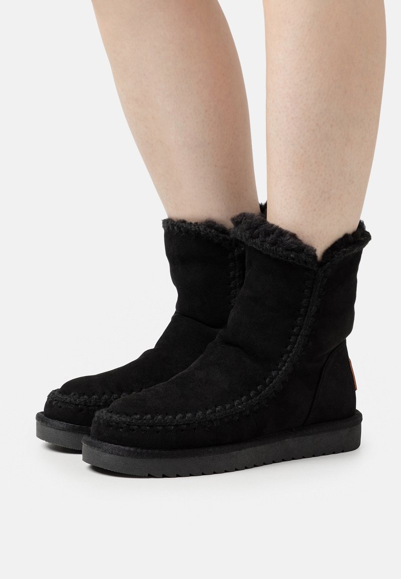 Las botas de tobillo de ante negro presentan un acabado texturizado, un borde de borrego en la parte superior y costuras en contraste a lo largo de las juntas. Suela de goma.