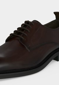 Σκούρο καφέ δερμάτινο επίσημο παπούτσι με κορδόνια, λείο φινίρισμα, στρογγυλή μύτη και μαύρη σόλα σε ανοιχτό φόντο.