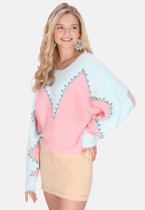 Colorblock sweater in lichtblauw en roze met een zigzagpatroon en decoratieve kralen langs de naden, gecombineerd met een beige rok.