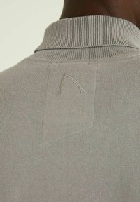 Polo en maille gris clair avec un col côtelé texturé et un détail de couture visible à l'arrière. Matière douce avec des éléments de design minimalistes.