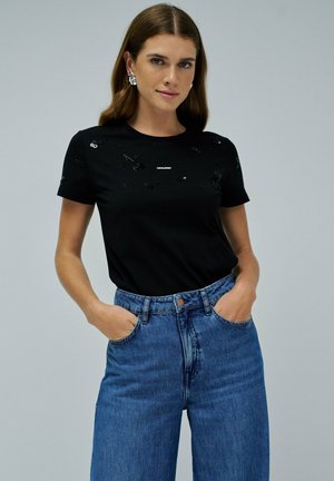 Camiseta negra de manga corta con adornos en el frente, combinada con jeans de mezclilla azules de tiro alto. Diseño limpio y casual.
