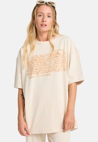 Beige oversized t-shirt lavet af blød bomuld, med et lys orange blomstermønster og teksten "Beach for Sunshine" trykt over brystet.