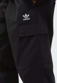 Pantalones cargo negros con un bolsillo de parche, con el logo blanco de Adidas en el lado izquierdo. Fabricados en una tela ligera y suave.