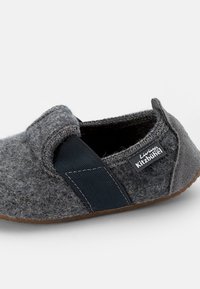Pantofole grigie in feltro con fascia elastica blu navy, suola in gomma e dettagli cuciti. Presenta un'etichetta laterale con il marchio "Living Kitzbühel".