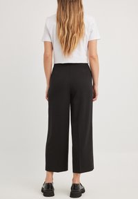 Zwarte wijde broek met een gladde textuur, hoge taille en gestructureerd ontwerp. Gepaard met een effen wit T-shirt met korte mouwen.