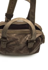 Sac en cuir brun avec double poignées, un dessus zippé et des détails texturés sur la sangle. Présente un subtil accent à franges.