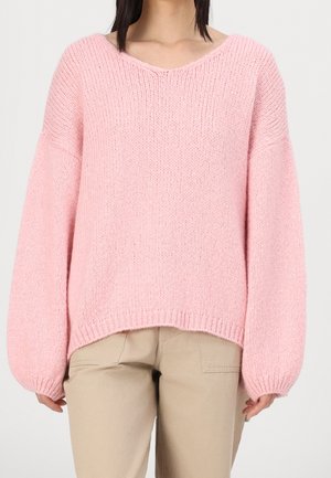 Rosa gestrickter Pullover mit V-Ausschnitt, lässiger Passform und weiten Ärmeln. Strukturierter Stoff mit gerippten Säumen, kombiniert mit beigefarbenen Hosen.