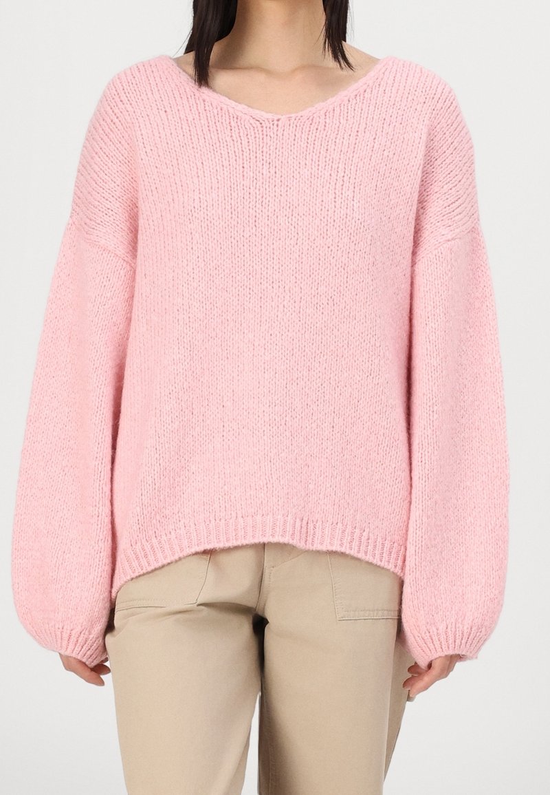 Maglione rosa lavorato a maglia con scollo a V, vestibilità rilassata e maniche larghe. Tessuto texturizzato con orli a coste, abbinato a pantaloni beige.