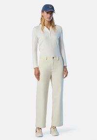 Top a maniche lunghe bianco a costine, pantaloni beige a gamba larga e berretto in denim blu. Sneakers bianche con dettagli rossi completano l'outfit.