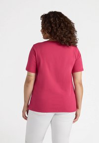 Camiseta de manga corta rosa hecha de tela suave, con un cuello redondo y dobladillo recto. La parte posterior tiene una textura suave sin detalles adicionales.