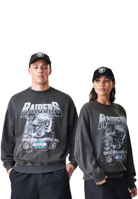 Sivá mikina z jogy s nápisom "Raiders" a grafikou Super Bowl Champions 1983. Obsahuje čiernu čiapku s tímovým logom, voľný strih a okrúhly výstrih.