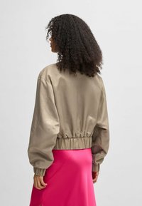 Khaki-bomberjakke med blank finish, som har puffærmer og rynket kant, parret med et rosa satin nederdel.