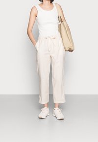 Pantalon beige léger avec une ceinture élastique et un cordon de serrage. Associé à un haut blanc sans manches et des baskets légères. Sac fourre-tout inclus.
