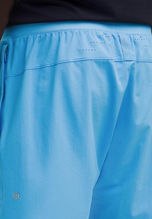 Close-up of a person wearing light blue athletic shorts with a black waistband and small ventilation holes near the top.