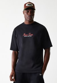 Μαύρη κοντομάνικη μπλούζα με κόκκινα γράμματα "New Era Buffalo, New York". Συνδυασμένη με έναν καφέ και πράσινο σκούφο με λογότυπο.