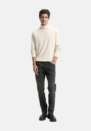 Hellbeiger Rollkragenpullover, weiche Textur; kombiniert mit dunkelgrauen Jeans und schwarzen Stiefeletten, einfacher und moderner Look.