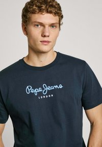 Jūras spēku zila kokvilnas t-kreklis ar gaiši zilu logo "Pepe Jeans London", kas izdrukāts centrā. Īsas piedurknes un apaļa kakla izgriezums.
