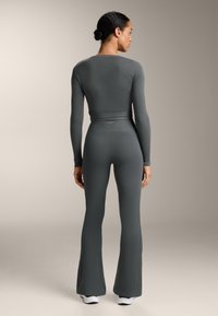 Sivi rebrasti top dugih rukava uparen s cipkastim tajicama, obje od rastezljivog materijala. Suptilan brending na pojasu. Minimalistički dizajn.