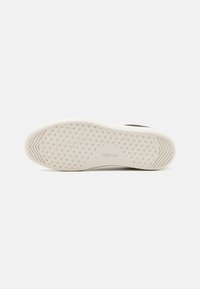 Die Sohle eines schwarzen Sneakers mit einer weißen, strukturierten Gummisohle, die geometrische Muster aufweist und das ALDO-Logo in der Mitte präsentiert.