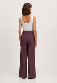Wijd gesneden broek in diep bordeauxrood, met een getailleerde pasvorm, hoge taille en achterzakken. Gepaard met een wit tanktop.