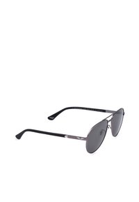 Lunettes de soleil aviateur à fine monture métallique avec verres teintés foncés et branches noires courbées reposant sur une surface blanche.