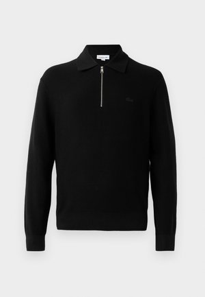 Zwarte gebreide pullover met een ritskraag, lange mouwen en een aansluitende onderkant. Heeft een subtiele logo op de borst. Gladde textuur.