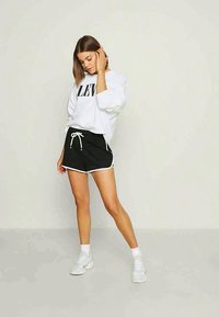 Sweatshirt branco com letras pretas, combinado com calções pretos com um acabamento branco nas laterais e cordão. Usado com ténis brancos.