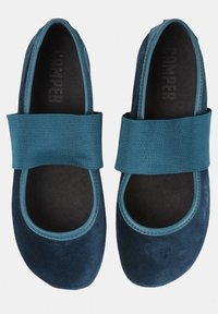 Blå mocka balettklackar med ett brett elastiskt band över fotryggen, rund tå och texturerad innersula, med varumärket "Camper" inuti.