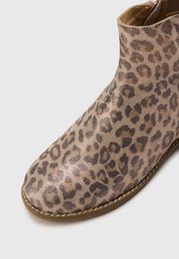 Botín de tobillo con estampado de leopardo, con una superficie texturizada y brillante, punta redonda y suela marrón en contraste, que cuenta con un cierre lateral con cremallera.