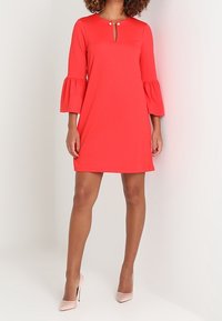 Rotes Kleid mit Glockenärmeln und Schlüssel-Ausschnitt, aus glattem Stoff gefertigt. Verziert mit dekorativen Knöpfen am Ausschnitt und einem knielangen Schnitt.