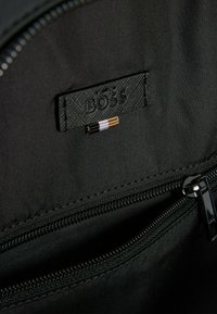 Interno in nylon nero con tasca con zip, caratterizzato da un'etichetta nera testurizzata in rilievo con la scritta "BOSS" e tre strisce orizzontali decorative.