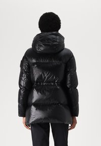 Sort pufferjakke med en blank finish, overdimensioneret hætte og quiltet design med indsnævret talje og sidelommer.
