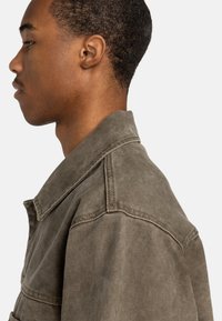 Olijfgroene denimjack met een kraag en zijzakken, met een gestructureerd oppervlak en zichtbare stiksels langs de naden.