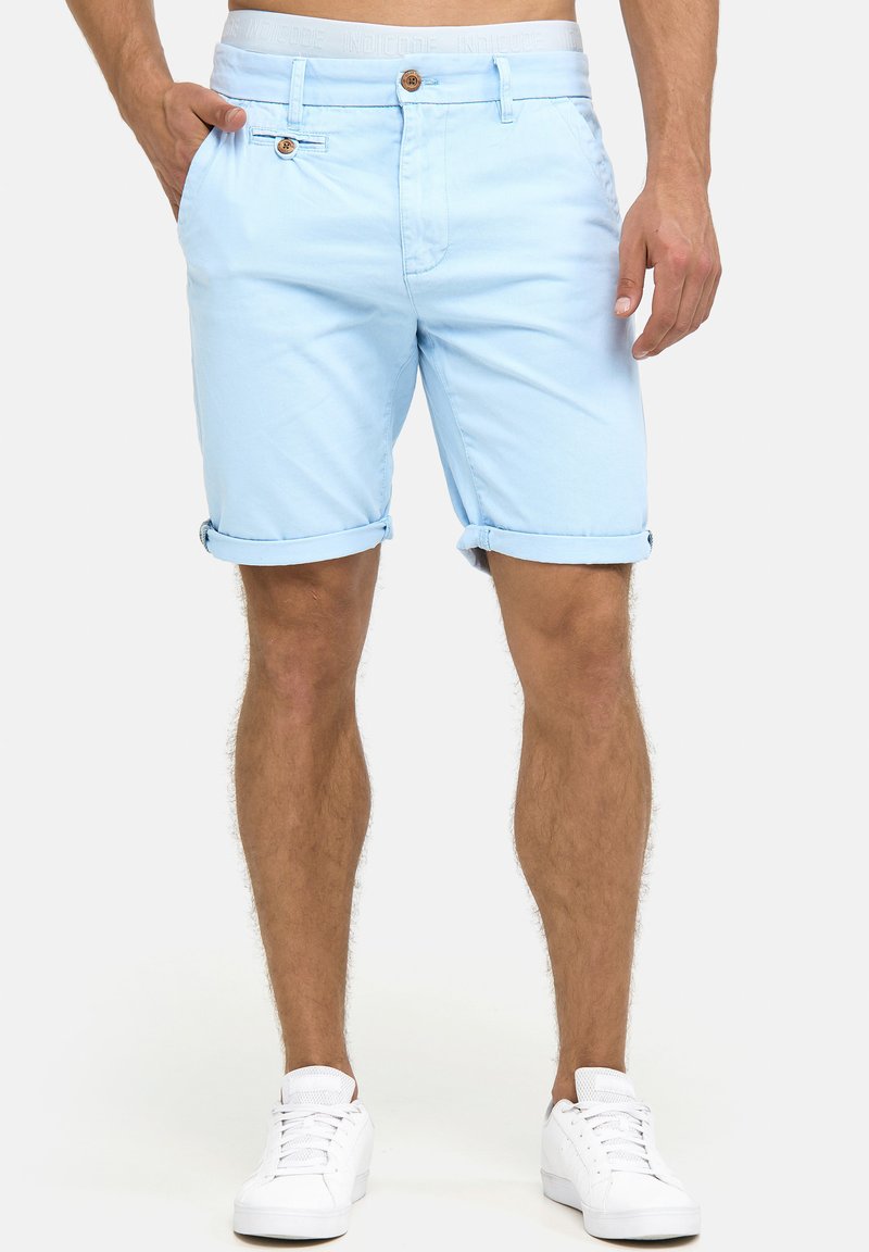 Lyseblå bomulds shorts med op rullede kanter, to sidelommer og knaplukning. Bæres med hvide sneakers.