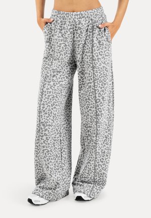 Partie inférieure vêtue d'un pantalon gris taille haute à larges jambes imprimé léopard avec poches côtés et baskets blanches sur fond uni.