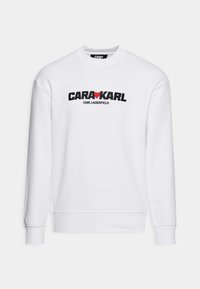Sudadera blanca con un gráfico bordado en negro y rojo que dice "CARA❤️KARL" y "KARL LAGERFELD" debajo. Diseño clásico de cuello redondo.
