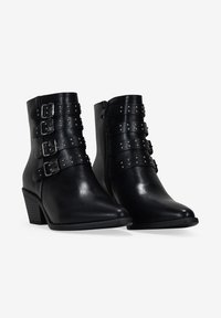 Bottines noires en cuir lisse avec cinq sangles réglables à boucles et des clous décoratifs. Bout pointu et talon bloc moyen.