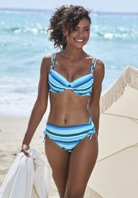 Dryžuotas bikinis mėlynos spalvos atspalvių. Brassiere turi lankelį, reguliuojamas trišaknius; aukštai juosmens apatinė dalis su šoninėmis nuorodomis. Minkšta medžiaga, paplūdimio aplinka.