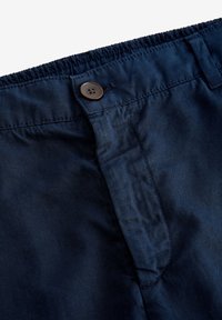Pantaloni corti blu navy con cintura elastica arricciata, chiusura con bottone marrone e tasche frontali piatte. Tessuto morbido con texture minima.