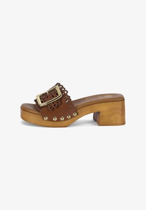 Sandale à enfiler en cuir marron avec talon bloc en bois, grande boucle dorée, bords festonnés et clous métalliques décoratifs le long de la semelle.