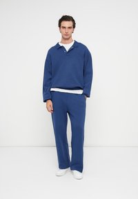 Modra bombažna sweatshirt z ovratnikom polo in tri gumbi, v kombinaciji s priložnostnimi ohlapnimi hlačami in belimi supergami.
