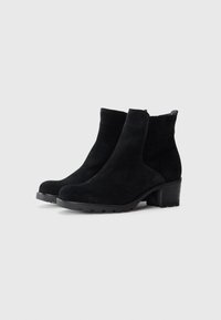 Par de botines de ante negro con tacones de bloque y suelas de goma en un fondo blanco liso.