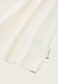 Helles, geripptes T-Shirt aus weichem Stoff mit abgerundetem Saum und einem kleinen Markenetikett an der Seite. Angenehme Textur und lockere Passform.