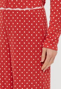 Rote gerippte Stoff-Loungewear mit weißen Punkten. Verfügt über einen dekorativen Spitzenrand an der Taille und lange Ärmel.