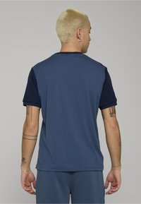 Granatowo-niebieska koszulka z krótkim rękawem i okrągłym dekoltem, wykonana z gładkiej tkaniny. Posiada jednolity kolor bez widocznych wzorów ani ozdób.