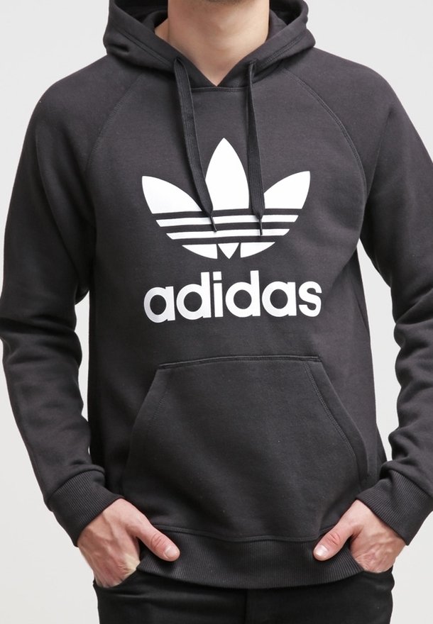 Svart huvtröja med en framficka, med en stor vit Adidas-logotyp och tre ränder ovanför logotypen. Tillverkad av mjukt material, ribbade muddars.