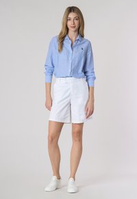 Camicia a maniche lunghe a righe blu e bianche abbinata a pantaloni corti bianchi e sneakers bianche. La camicia ha un colletto con bottoni e una vestibilità rilassata.