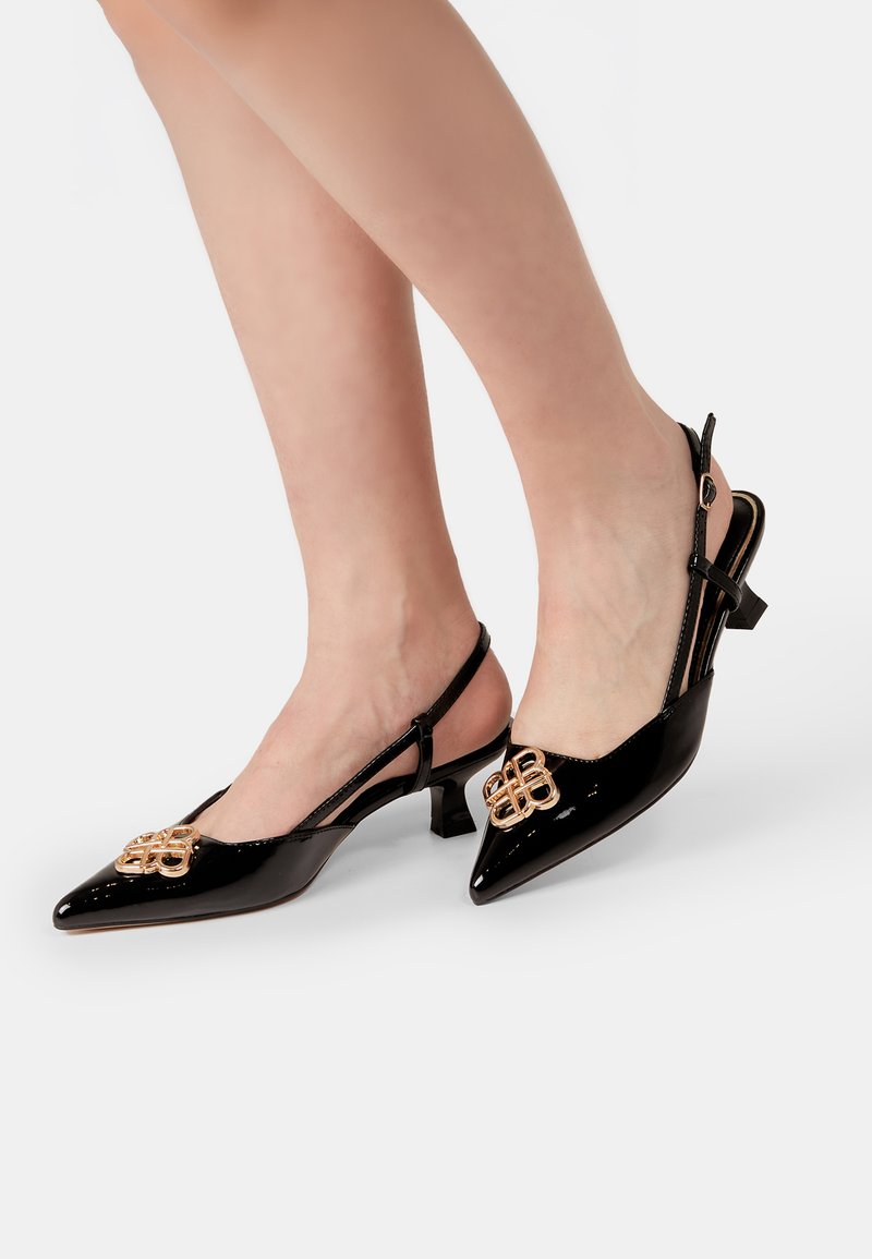 Črne patentne slingback pete s koničastim nosom, nizkim blokastim petam in zlatim okrasnim elementom spredaj. Gladka tekstura.