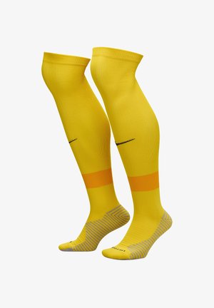 Calze gialle fino al ginocchio con righe arancioni, motivo testurizzato di grip sulla parte del piede e un logo nero di lato. Realizzate in materiale elastico.