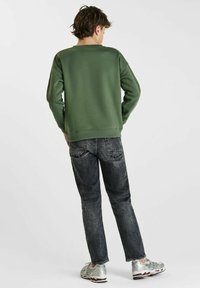 Groene sweatshirt met een ronde hals en geribde manchetten, gecombineerd met donkere spijkerbroeken. Reflecterende zilveren sneakers maken de outfit compleet.